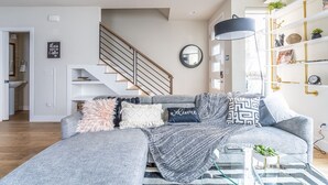 A modern living room with a grey sofa, a staircase, a bookshelf, and a coffee machine. - 4BR | BBQ, Rooftop | Eastlake | Sophari Home C (Seattle)