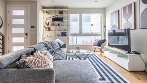 A living room with a sofa, TV, and bookshelf. - 4BR | BBQ, Rooftop | Eastlake | Sophari Home C (Seattle)