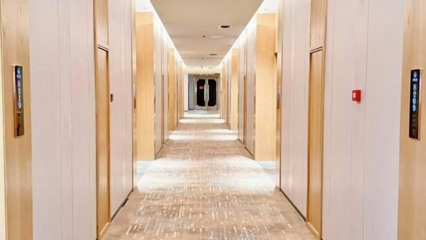 Un largo y estrecho pasillo de hotel con puertas a ambos lados y piso alfombrado.