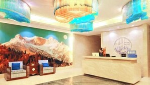 Zona de recepción de hotel con un mural de montañas, un mostrador de recepción y un área de descanso con piso estampado.