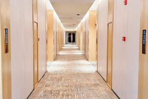 A hotel corridor with a carpeted floor, doors on both sides, and a light-colored ceiling.