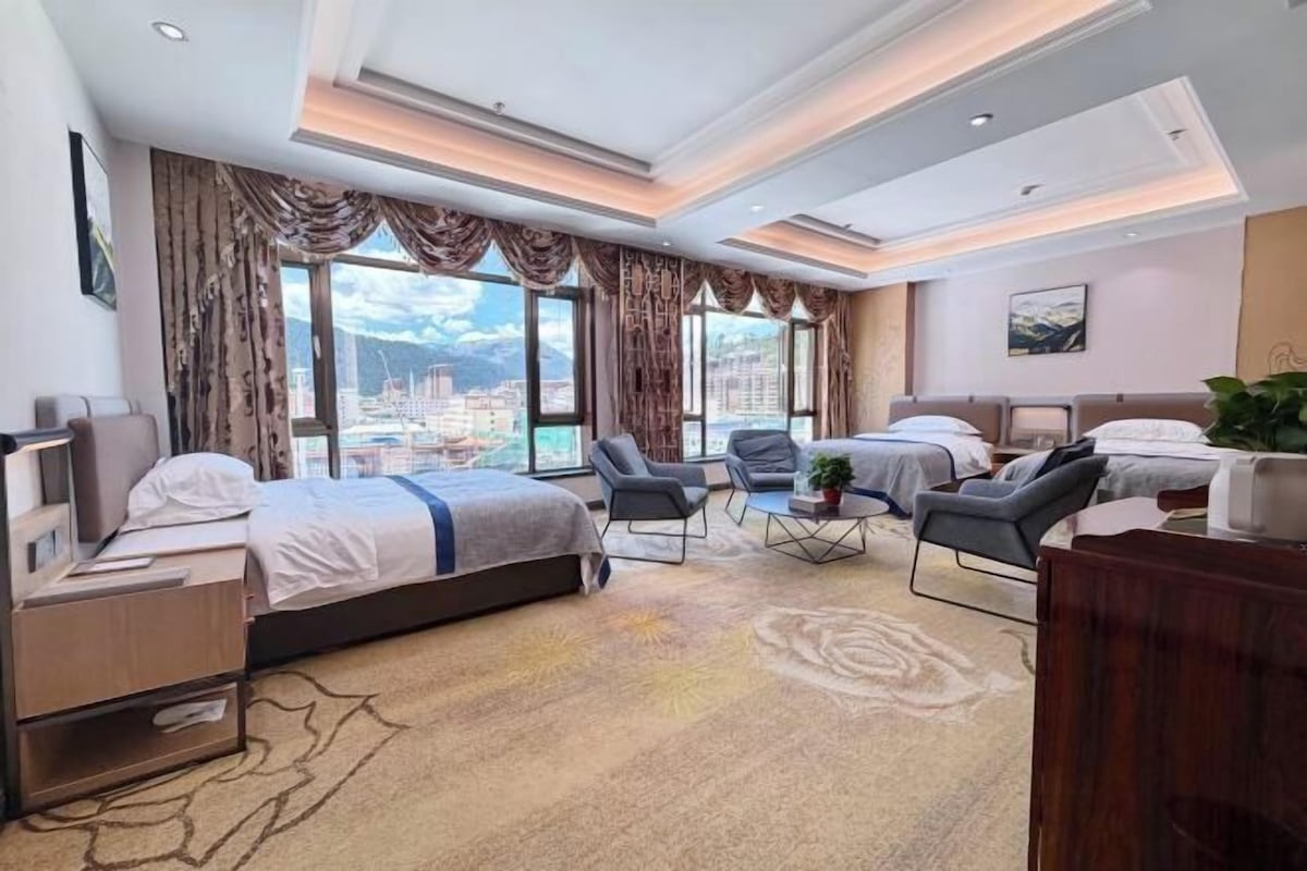 Une chambre d’hôtel avec un grand lit, deux fauteuils, un bureau et une vue sur la ville.
