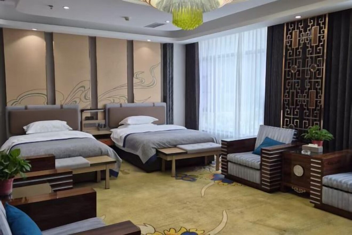 Une chambre d’hôtel avec deux lits, un canapé, une petite table et une plante en pot.
