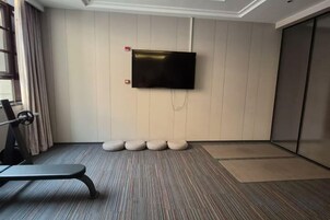 A hotel room with a flat-screen TV mounted on the wall, a bench, and a set of round ottomans.