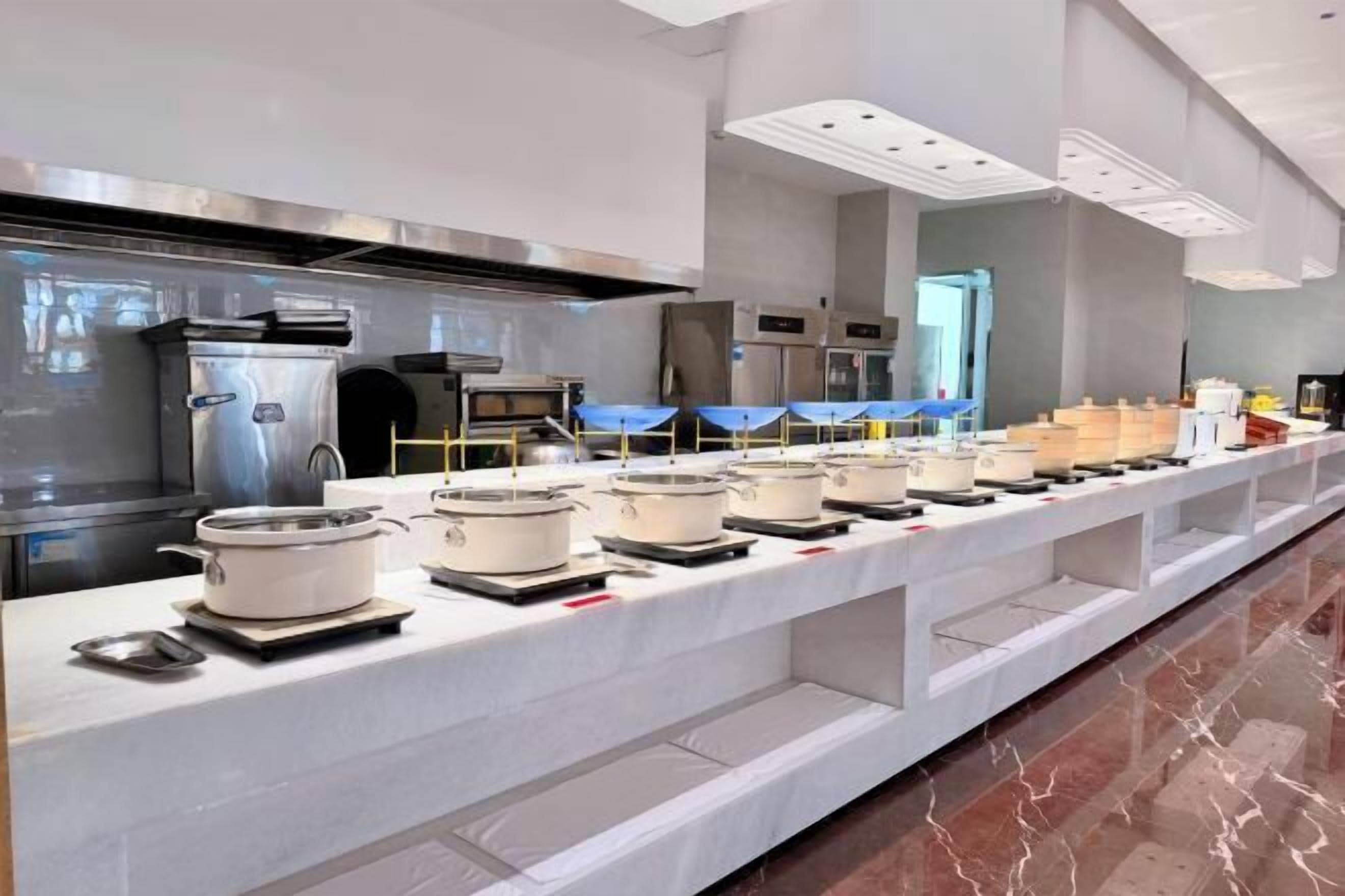 A buffet setup with multiple serving stations, stainless steel appliances, and a marble floor.