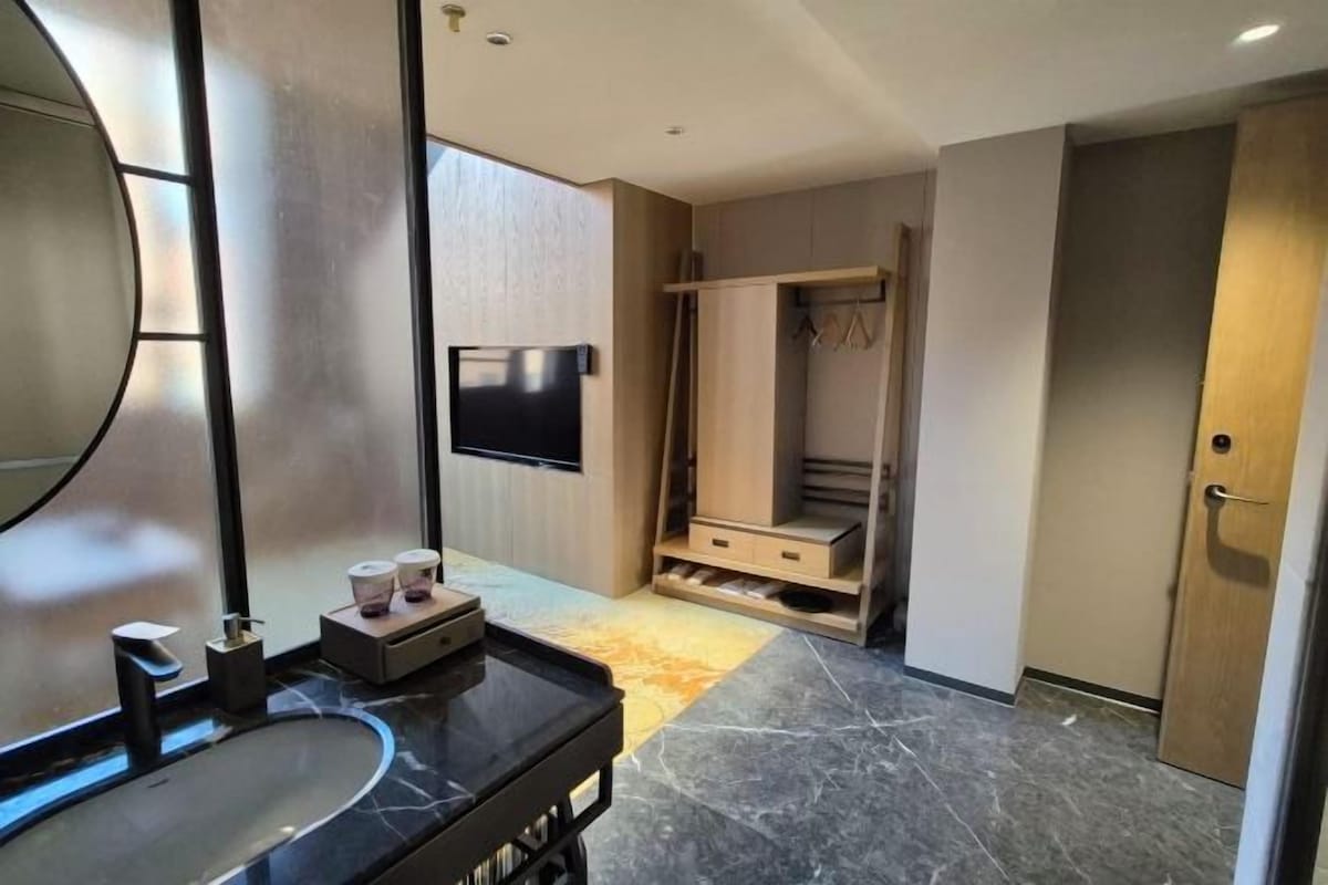 Une salle de bain moderne avec un grand miroir, un plan de toilette noir, un téléviseur et une douche à l’italienne.