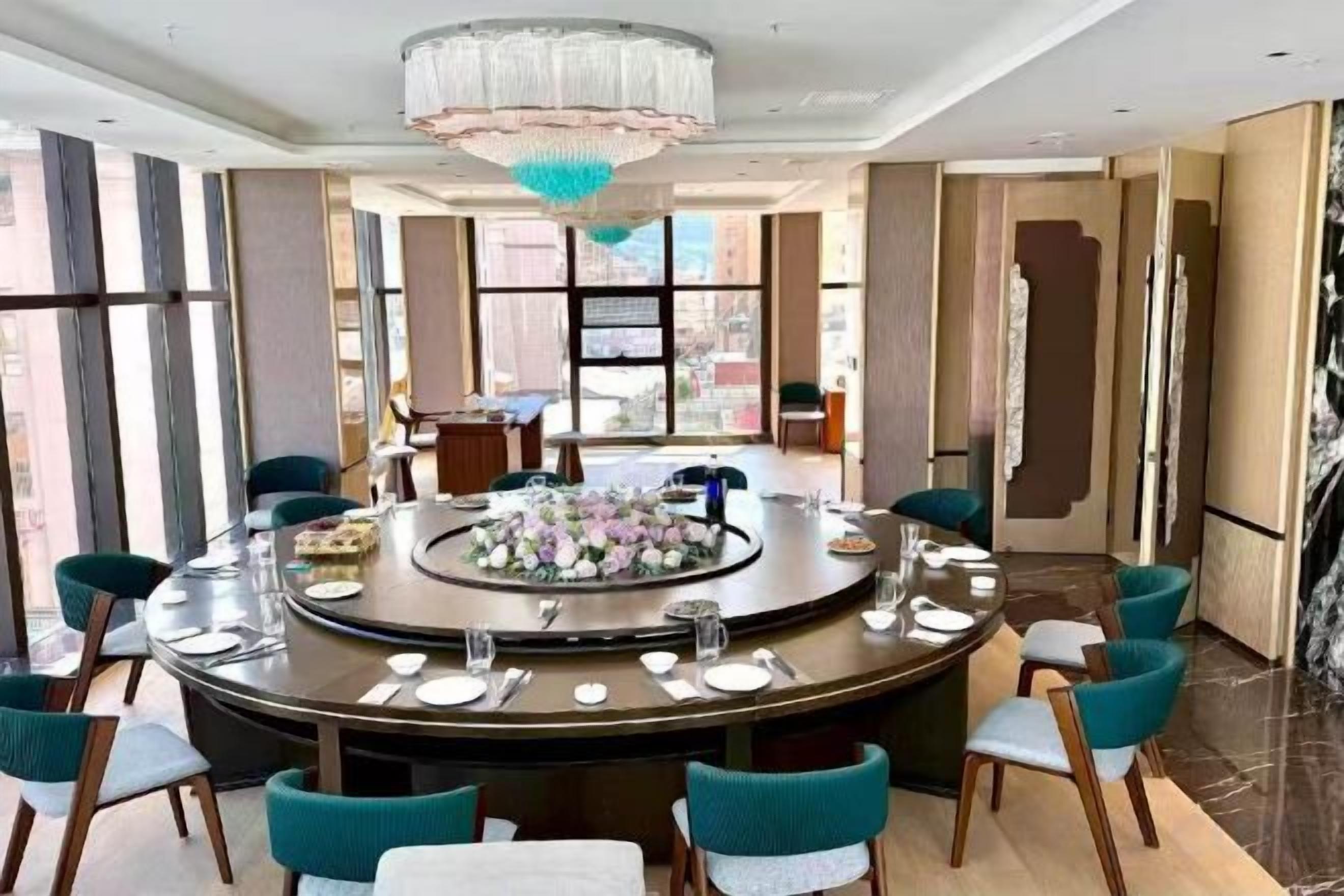 A round dining table with chairs, a chandelier, and a view of the city.
