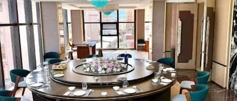 A round dining table with chairs, a chandelier, and a view of the city.