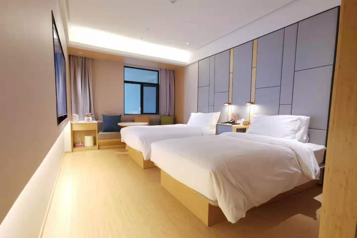 A hotel room with two beds, a desk, a chair, a window with curtains, and a flat-screen TV.
