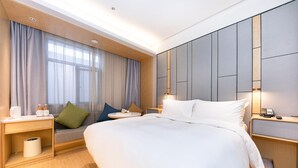 Una habitación de hotel moderna con una cama grande, una mesita de noche y una ventana con cortinas.