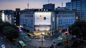 Un hotel con un cartel grande que anuncia iPhone y Apple Watch, rodeado de edificios modernos y una calle concurrida.