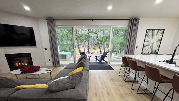 Una sala de estar moderna con chimenea, un sofá gris y un comedor con taburetes de bar.
