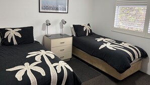 A bedroom with two beds, a nightstand, a drawer unit, a framed picture on the wall, and a window with blinds. - MANLYS FINEST LOCATION SO CLOSE TO BEACH SHOPS AND FERRY  (Manly)