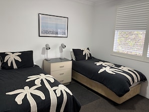 A bedroom with two beds, a nightstand, a drawer unit, a framed picture on the wall, and a window with blinds.