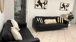 A living room with a black sofa, a black armchair, and a black leather couch. There are abstract paintings on the wall and a potted plant. - MANLYS FINEST LOCATION SO CLOSE TO BEACH SHOPS AND FERRY  (Manly)