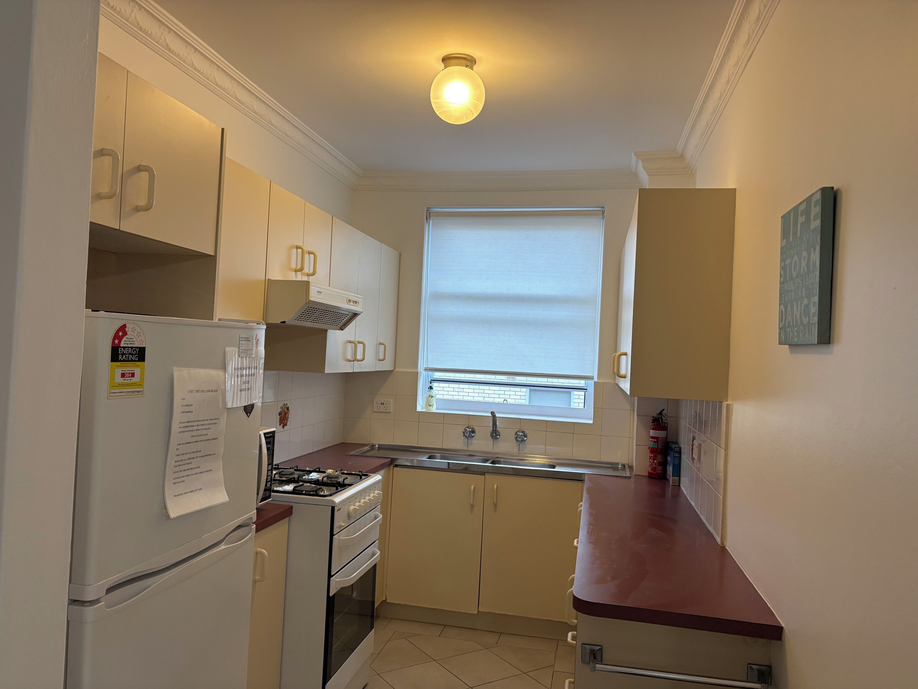 A compact kitchen with white cabinets, a gas stove, a refrigerator, and a window with blinds.