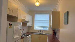 A compact kitchen with white cabinets, a gas stove, a refrigerator, and a window with blinds. - MANLYS FINEST LOCATION SO CLOSE TO BEACH SHOPS AND FERRY  (Manly)