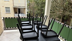 A row of black chairs with a table in an outdoor area with a tiled floor, surrounded by a green fence, and a building in the background. - MANLYS FINEST LOCATION SO CLOSE TO BEACH SHOPS AND FERRY  (Manly)