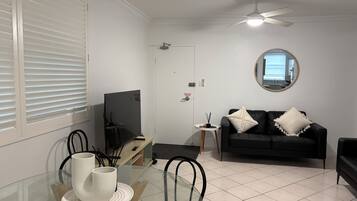 A living room with a TV, a black sofa, a round mirror, and a dining area with chairs and a table.