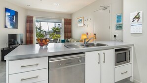 Una cocina moderna con lavavajillas integrado, microondas y fregadero. Hay un cuenco de fruta en la encimera y una ventana con cortinas.