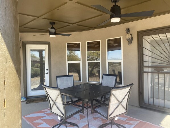 Une terrasse couverte avec une table et des chaises, des ventilateurs de plafond et des fenêtres.