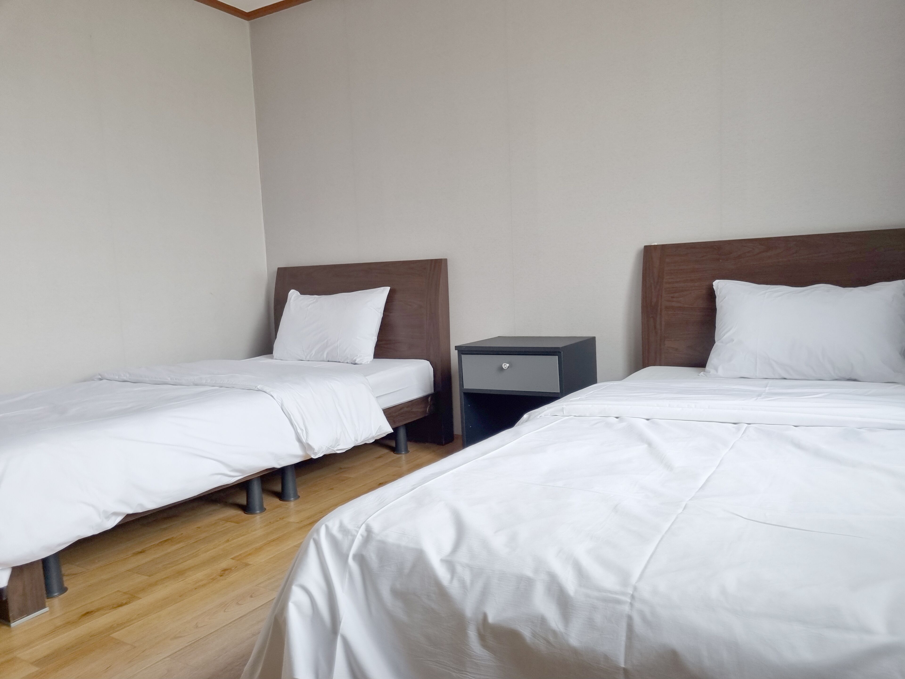 Hotellihuone, jossa on kaksi erillistä sänkyä, puiset päätyosat, valkoiset vuodevaatteet, pieni yöpöytä ja yövalaisin.
