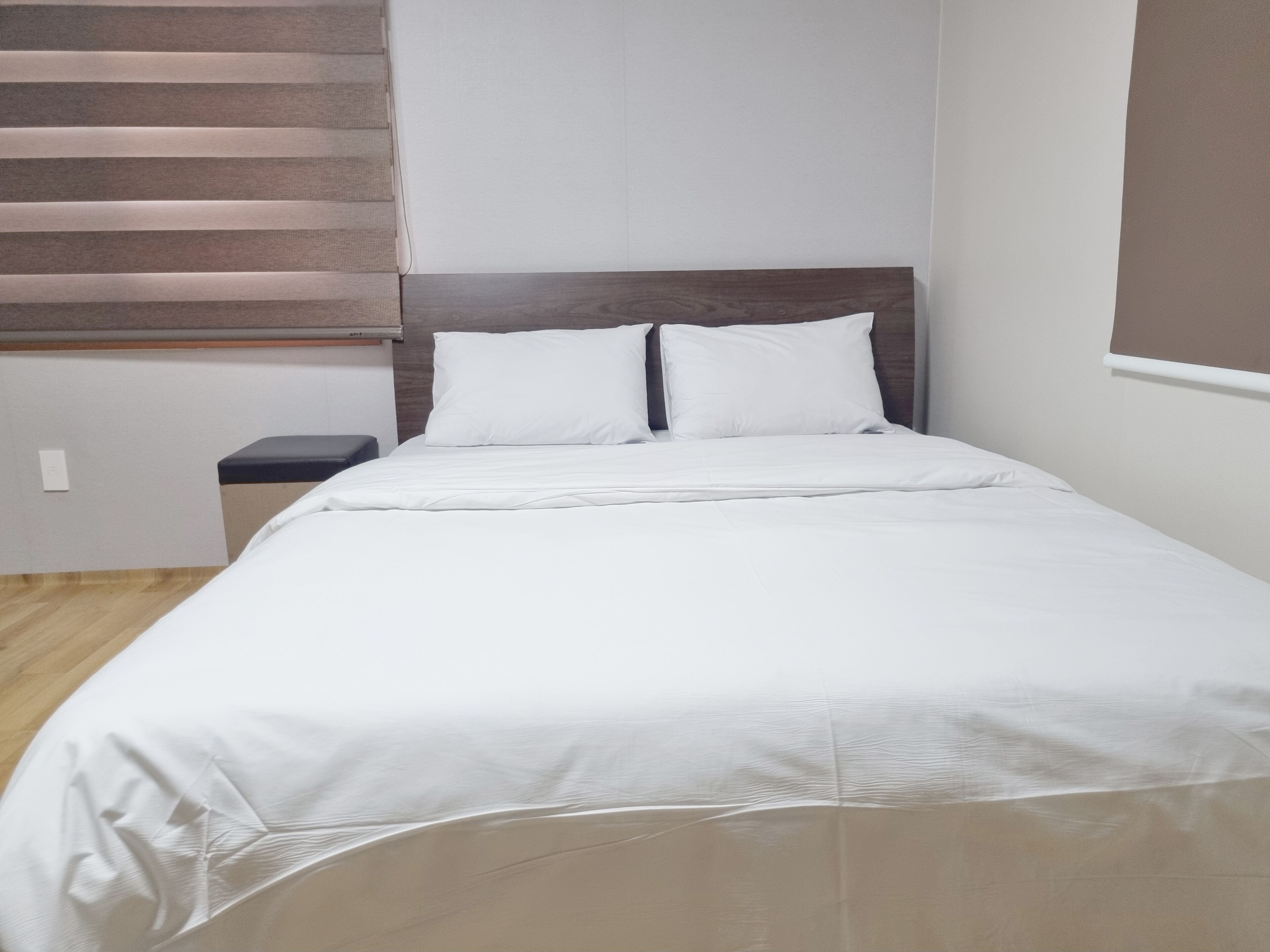 A neatly made bed with white bedding in a room with a wooden floor and a headboard with horizontal slats.
