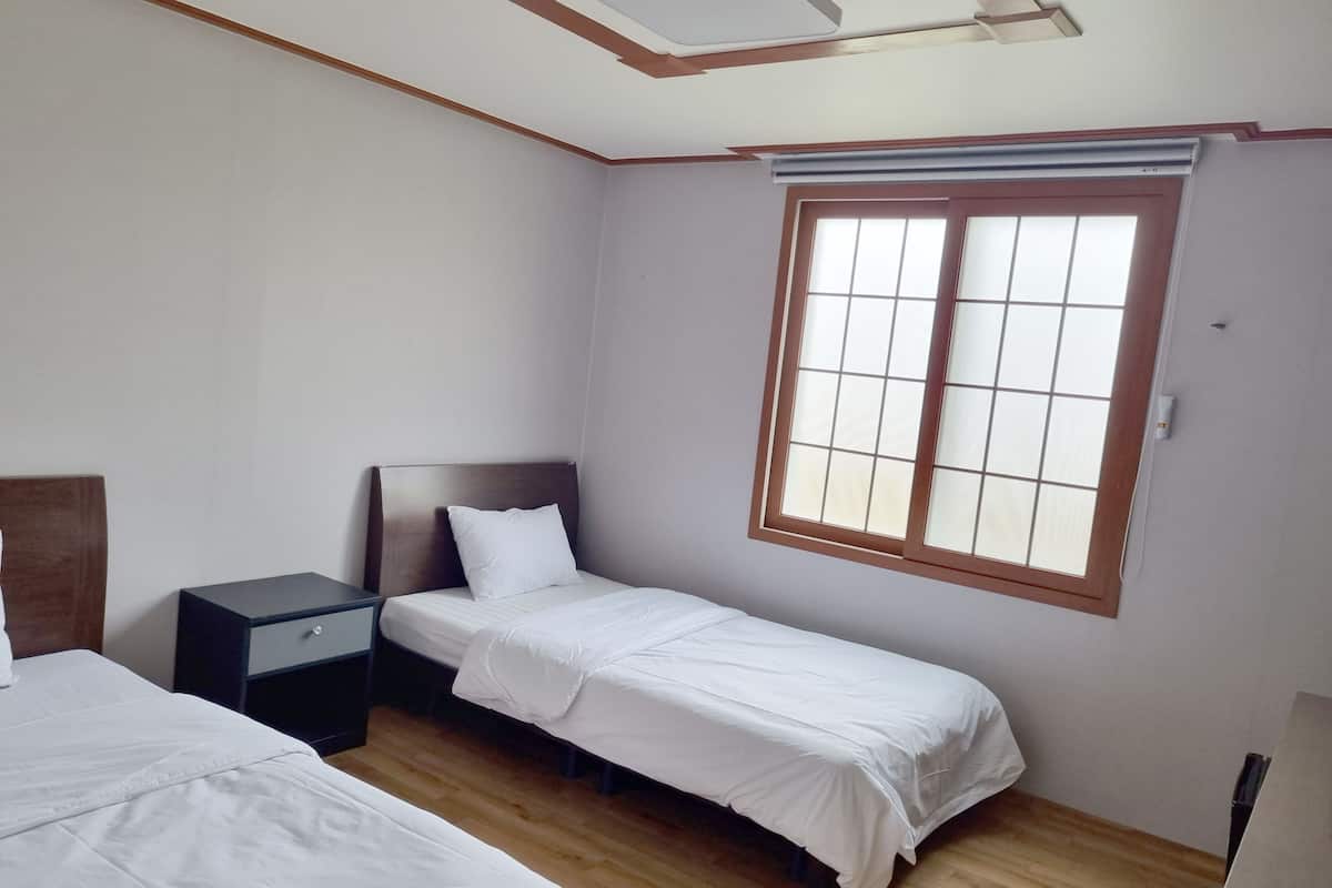A room with two beds, a nightstand, and a window with blinds.