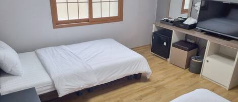 A hotel room with two single beds, a desk with a computer, a TV, a small fridge, and a trash bin.