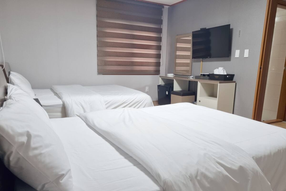 A hotel room with two beds, a desk, a television, and a window with blinds.