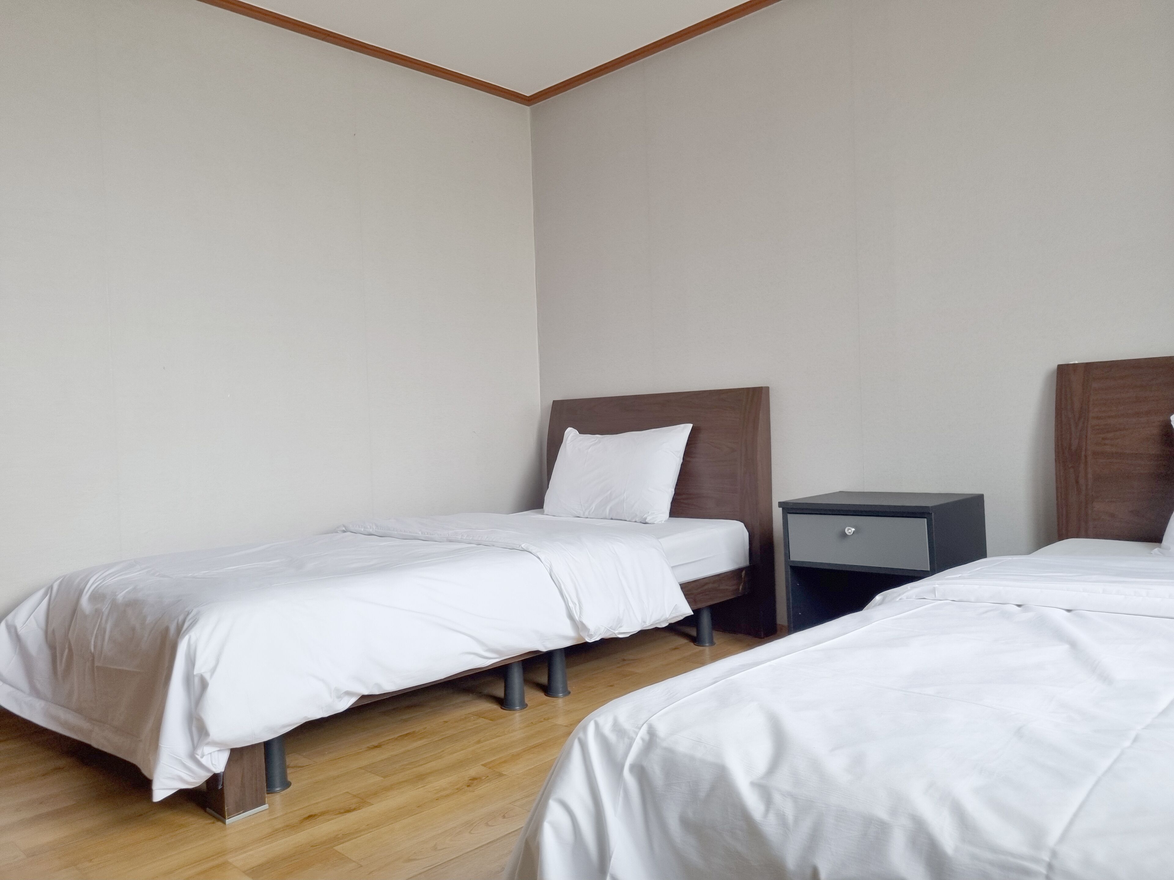 Une chambre d’hôtel avec deux lits simples, une petite table de chevet et un plancher en bois.