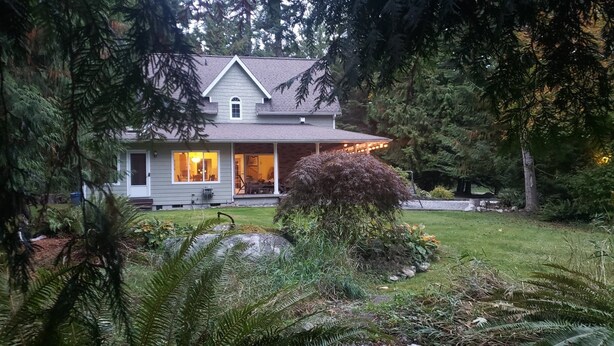 A two-story house with a covered porch, surrounded by dense greenery and trees.