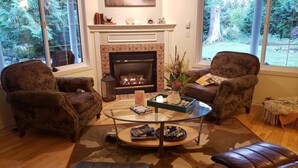 A cozy living room with a fireplace, two armchairs, a glass coffee table, and a view of the outdoors.