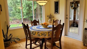 A dining area with a round table, chairs, a chandelier, a window with a view of trees, and a door with a wreath.