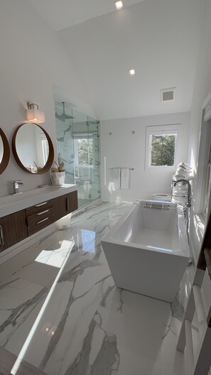 Un baño moderno con una bañera grande, cabina de ducha de vidrio y tocador con espejo.