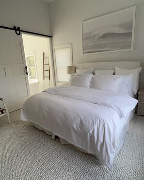 Un dormitorio espacioso con una cama grande, una escalera, una puerta, una lámpara de pared y un cuadro.