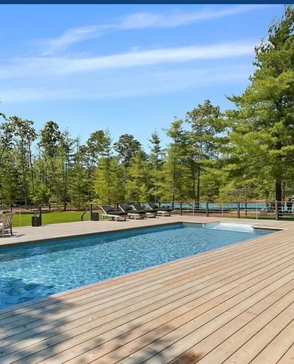 Una piscina rectangular con cubierta de madera, rodeada de árboles y un cielo despejado.