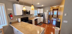 A modern kitchen with white cabinets, stainless steel appliances, and pendant lighting. - Sandsation: Direct Dune Access, Lakefront & Trailer Parking (North Bend)