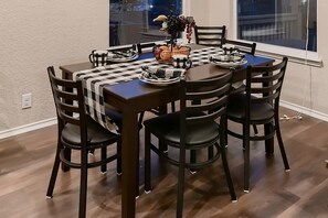 Een eettafel compleet met stoelen, een geruit tafelkleed en een fruitmand.