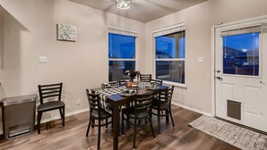 A dining area with a table set for six, surrounded by chairs, with a view of the outside through large windows. - Lxry 4 BR, Heated Pool/Spa, Large Game Room, near Seaworld/Six Flags (St1) (San Antonio)