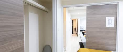 A modern hotel room with a bed, a wardrobe, and a door leading to a hallway.