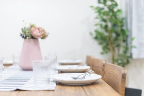 A dining table set with plates, cutlery, and glasses, accompanied by a pink vase with flowers.