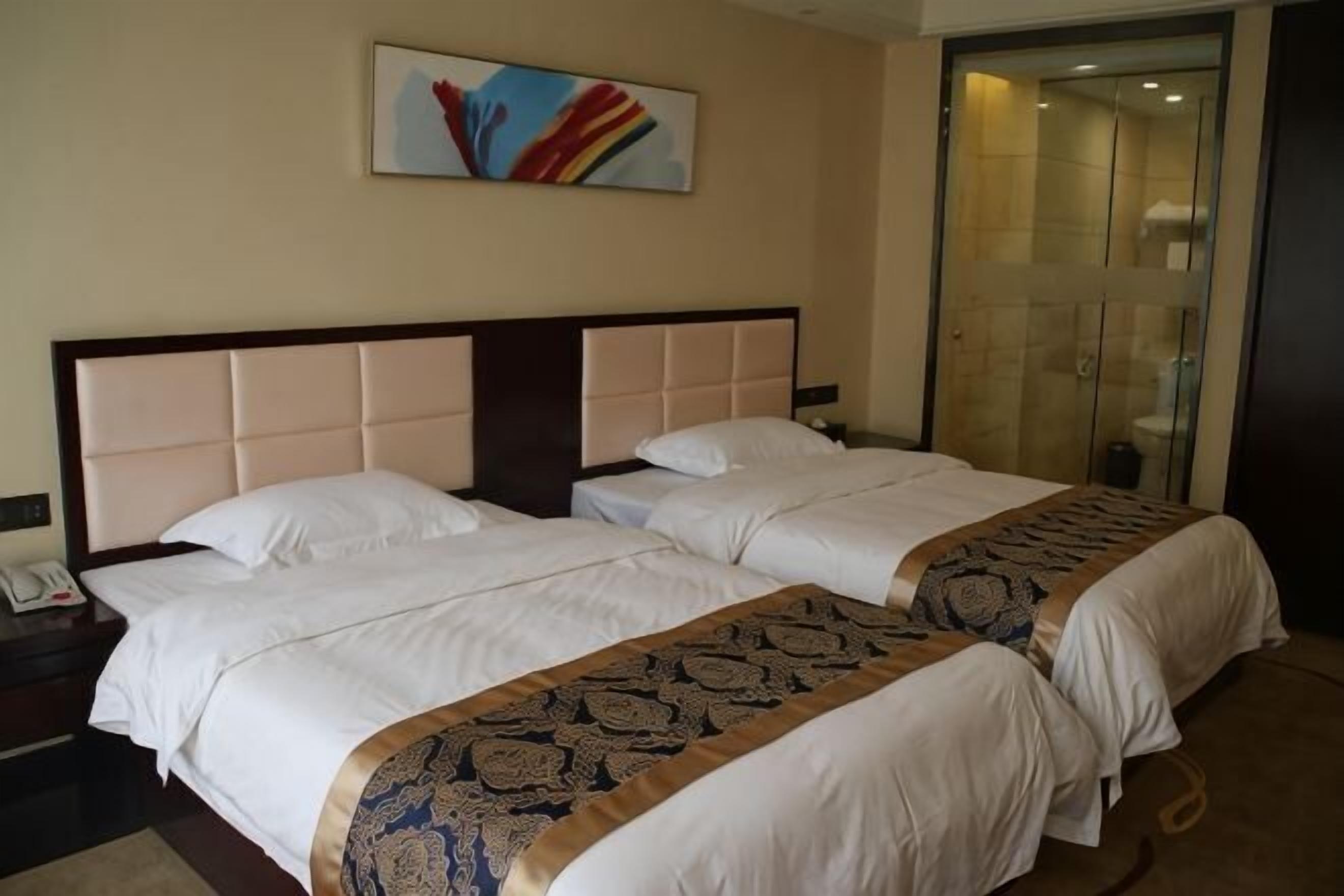 A hotel room with two beds, a bedside telephone, and a glass-enclosed shower area.