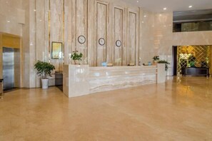 A reception area with a marble reception desk, vertical wooden panels, and potted plants.