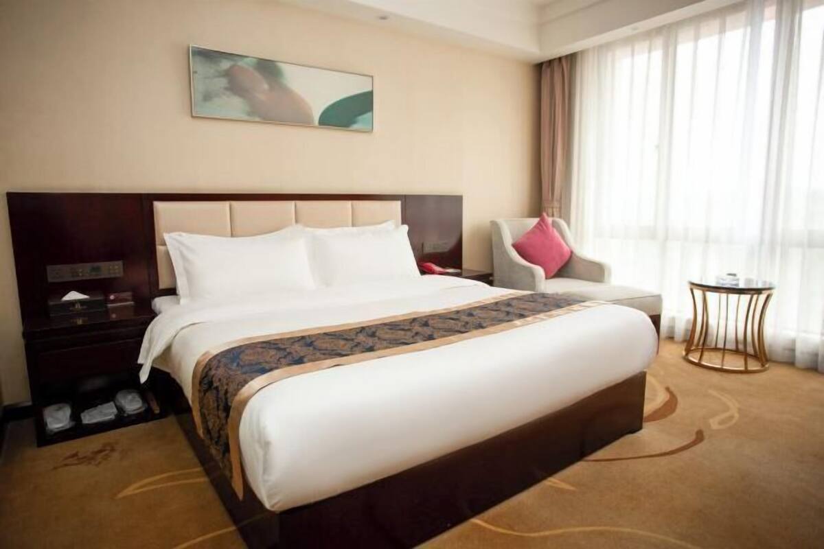 Una habitación de hotel con una cama grande, una mesita de noche, una silla, una pequeña mesa y una ventana con cortinas.
