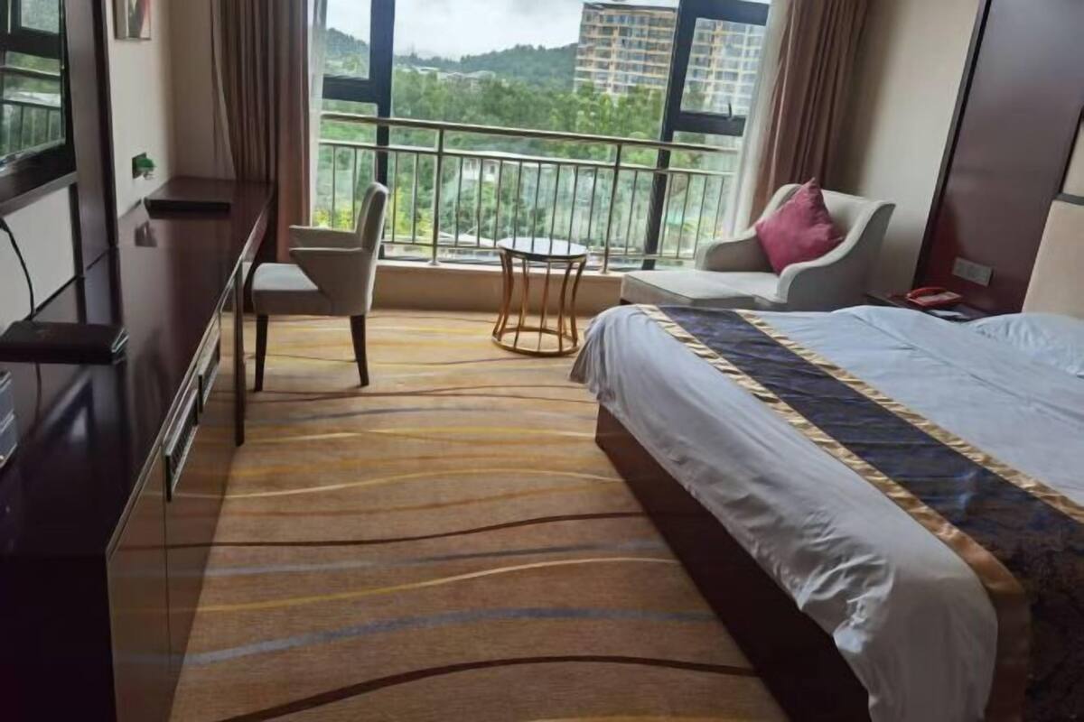 Una habitación de hotel con cama, escritorio, silla, una mesita y un balcón con vista a la ciudad.