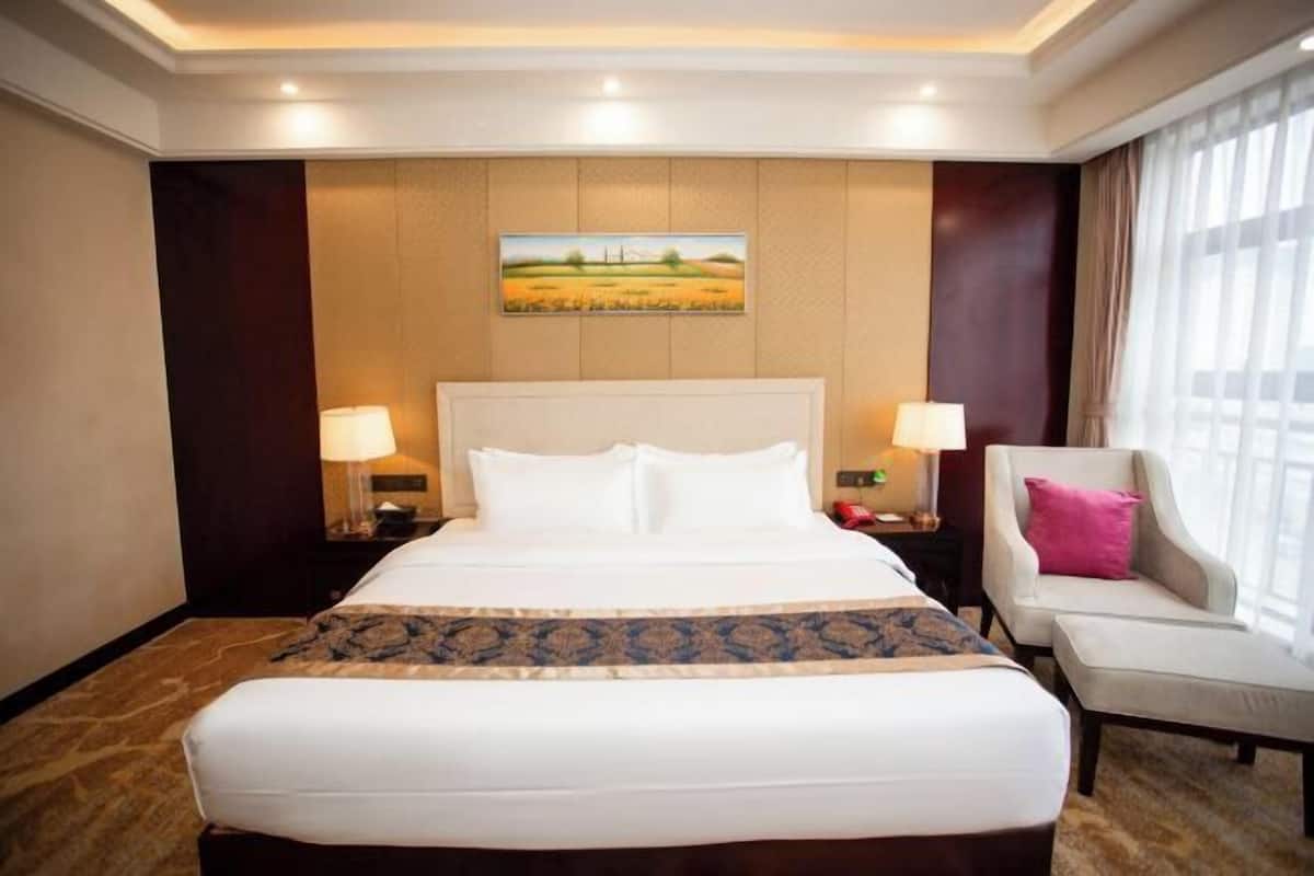 Habitación de hotel con una cama grande, dos mesitas de noche con lámparas, una silla y un cuadro en la pared.