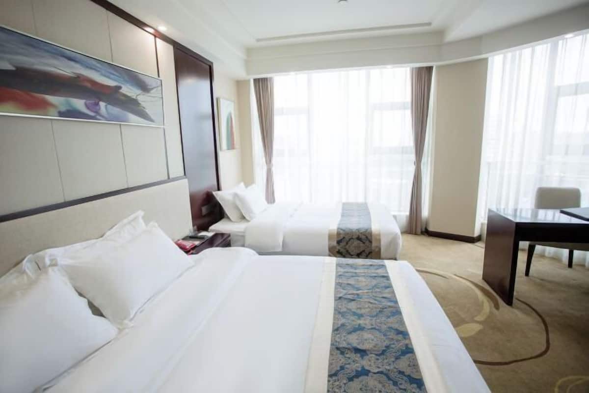 Una habitación de hotel con dos camas, un escritorio y un ventanal con cortinas.