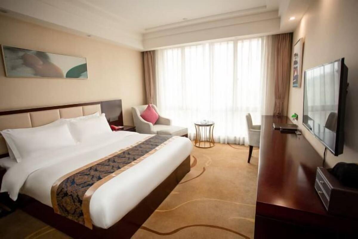 Habitación de hotel con una cama grande, un escritorio con televisor de pantalla plana, una silla, una mesita y un ventanal con cortinas.