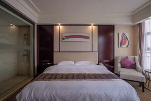 Een hotelkamer met een groot bed, een nachtkastje, een stoel en een douchecabine van glas.